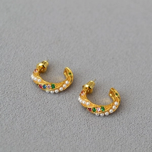 Macro detail of gold-plated twisted C-shaped earrings with colorful zircons and pearls