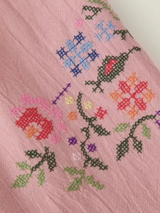 Vista macro di ricami floreali colorati su tessuto di cotone rosa con cuciture fini