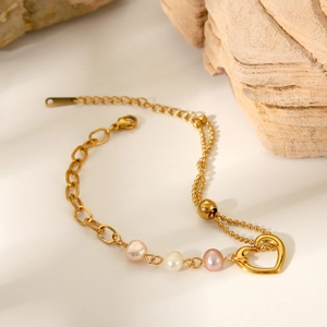 Detailed view of a gold heart pendant bracelet with natural pearls on a stone background