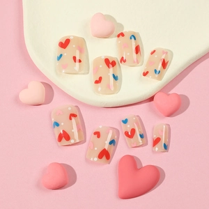 Press on nails with red and blue hearts on nude base displayed on a pink background