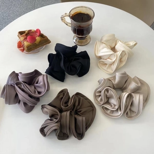 Detail view of five assorted satin scrunchies in earth tones on a white table