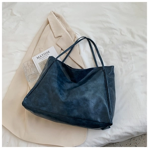 Detail of a large navy blue faux leather tote bag on a white bedsheet with a book