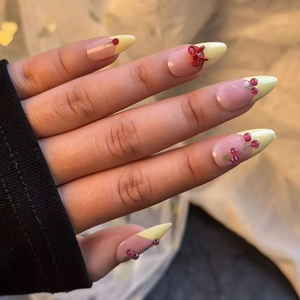 Detail of French almond press-on nails with 3D cherry charms and red bows