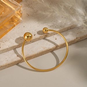 Detailed macro of golden stainless steel open cuff bangle on natural travertine stone