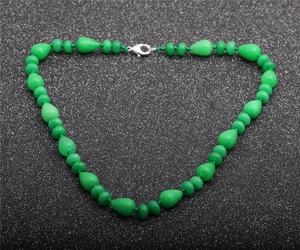 Detail of green tiger eye and opal teardrop beads with metallic clasp on dark surface