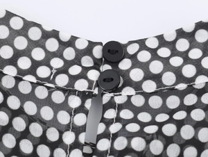 Macro view of black and white polka dot chiffon fabric with black button fastening detail