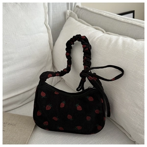 Close-up of black corduroy shoulder bag with red strawberry embroidery and ruffled handle