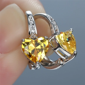 Close-up of fingers holding heart-shaped yellow zircon earrings in white gold plating
