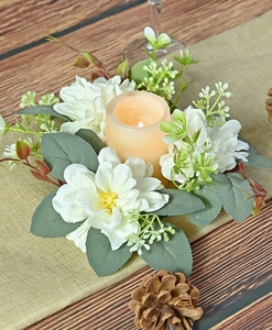 Close-up of dahlia candle ring with white flowers and a glowing LED candle on a table