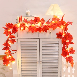 Macro detail of warm LED light string with red maple leaves on a white cabinet