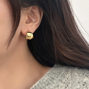 Close-up of a chunky gold hoop earring with polished metallic finish on model ear
