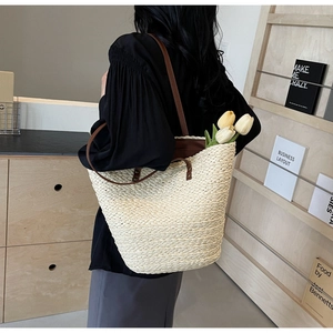 Model wearing large beige straw tote bag with brown leather straps in indoor setting