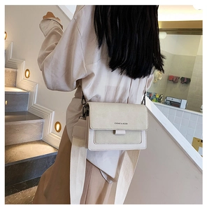 Detail of a chic off-white crossbody bag with wide strap on a model in a warm interior