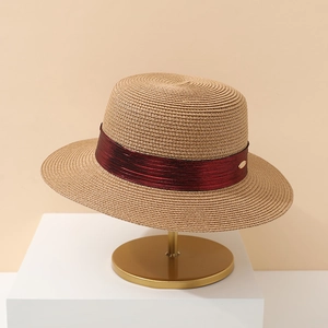 Detail of handwoven straw hat featuring a dark red ribbon and a golden metal logo plate
