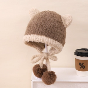 Dettaglio del cappello di peluche con paraorecchie, maglia morbida e pompon marroni soffici