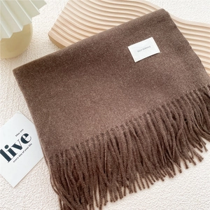 Detailed texture of thick dark brown knit scarf with fringe tassel on wooden tray