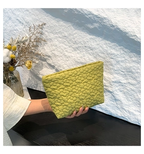 Detailed close-up of green floral quilted fabric texture on a soft fashion clutch bag