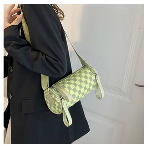Close-up of light green checkerboard cylinder bag with wide fabric strap on model