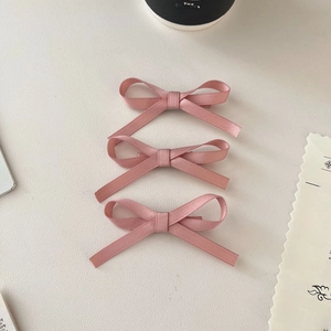 Detail view of 3pcs pink satin bow hair clips on a minimalist light-colored surface