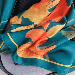 Detail of silk-like scarf featuring deep green base with orange blossoms and leaf pattern
