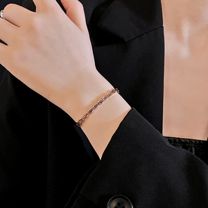 Close-up of a model wearing a gold bracelet with oval purple gemstones on a black suit