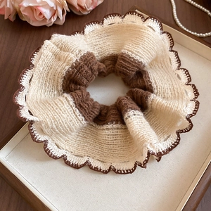 Close-up of oversized knitted scrunchie with lace trim on a decorative wooden tray