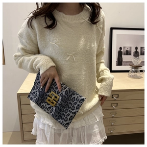 Detail of leopard print clutch with gold H-buckle styled with a cream bow sweater