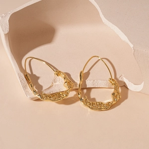 Detail view of golden irregular oval earrings with lava texture on stone pedestal