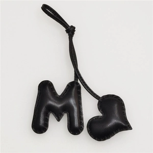 Close-up of black leather M-letter and heart charm with refined hand-stitched detailing