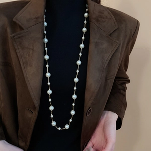 Detail of long pearl necklace with golden chain on a model wearing a brown blazer