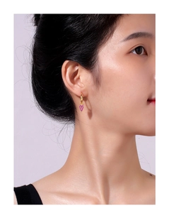 Detailed close-up of heart-shaped gold earrings with purple zircon on a female model