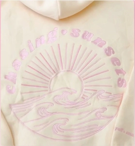 Detail of 3D digital print with chasing sunsets text and sun waves on yellow hoodie
