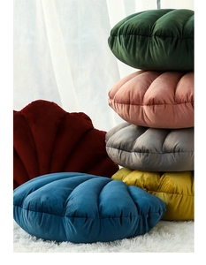 Detail of shell-shaped velvet pillows in multiple colors stacked on a cozy white rug