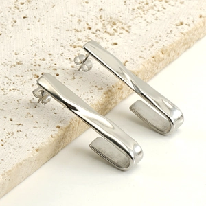 Sleek silver hook-shaped stainless steel earrings on a textured stone surface