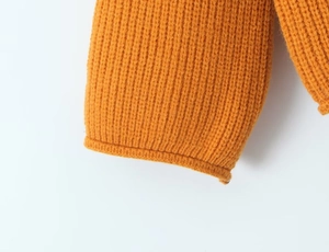 Vue détaillée de la texture du tricot orange et de la finition du poignet d'un pull