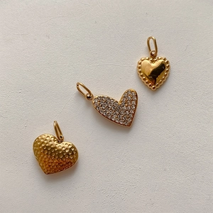 Three heart-shaped pendants in gold finish with polished, hammered, and paved textures