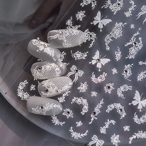 Detail of white lace nail stickers with floral patterns and butterfly rhinestone accents