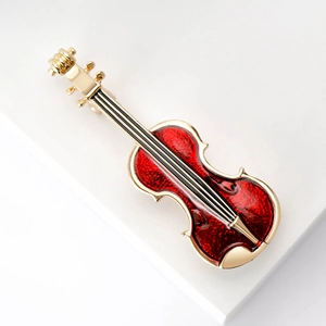 Detailed view of a violin brooch with golden metal edges and vibrant red enamel finish