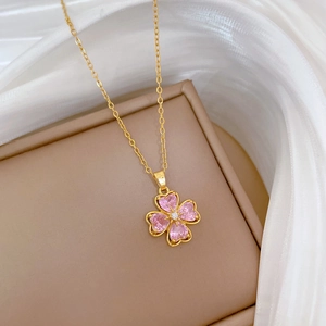 Macro detail of a gold clover necklace with pink heart crystals on silk fabric