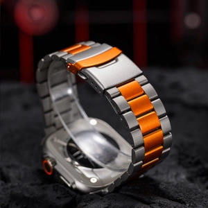 Macro shot of titanium gray and orange metal watch band on a textured rock surface