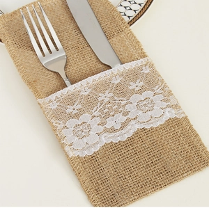Detail of burlap cutlery holder with white lace trim and metal fork on rustic table