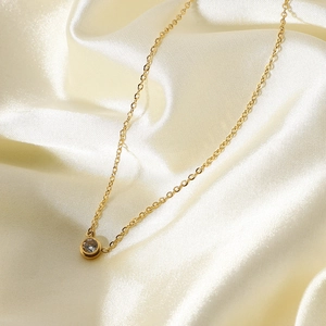 Close-up of minimalist gold necklace with round zircon pendant on white silk fabric