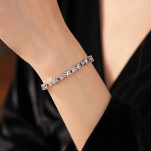 Dettaglio del bracciale a X in argento con zirconi blu al polso su tessuto scuro