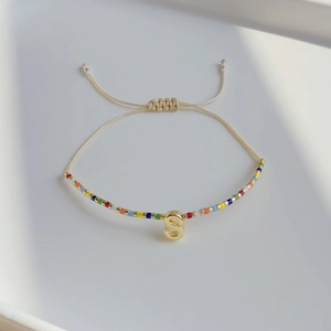 Detailaufnahme des handgefertigten Perlenarmbands mit goldenem S-Anhänger und Kordel
