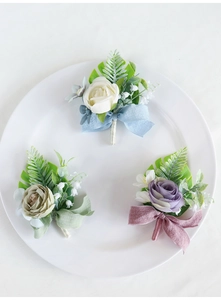 Close-up of wedding boutonnieres with silk roses in cream, green and purple on white ceramic