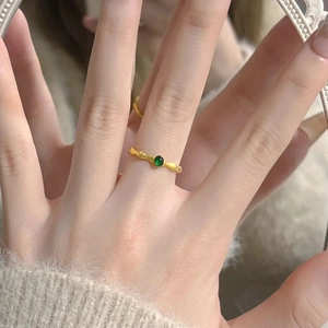 Detail of gold bamboo-shaped ring with a green gemstone worn on a finger