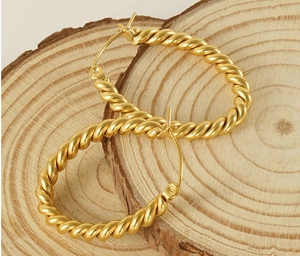 Macro view of gold twisted oval earrings on a natural wood surface showing metal texture