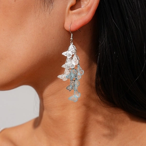 Detailed close-up of hollow butterfly tassel earrings in silver and blue on a model