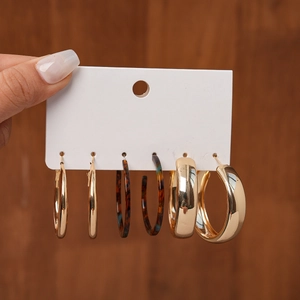 Detailed set of metallic hoops and tortoise resin earrings on a wooden background