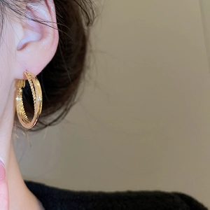 Close-up of a woman wearing gold twisted multi-layer hoop earrings with metallic finish